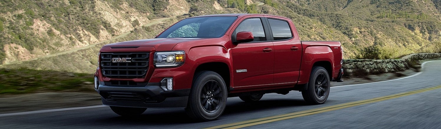 Red GMC pickup truck driving on a scenic mountain road.