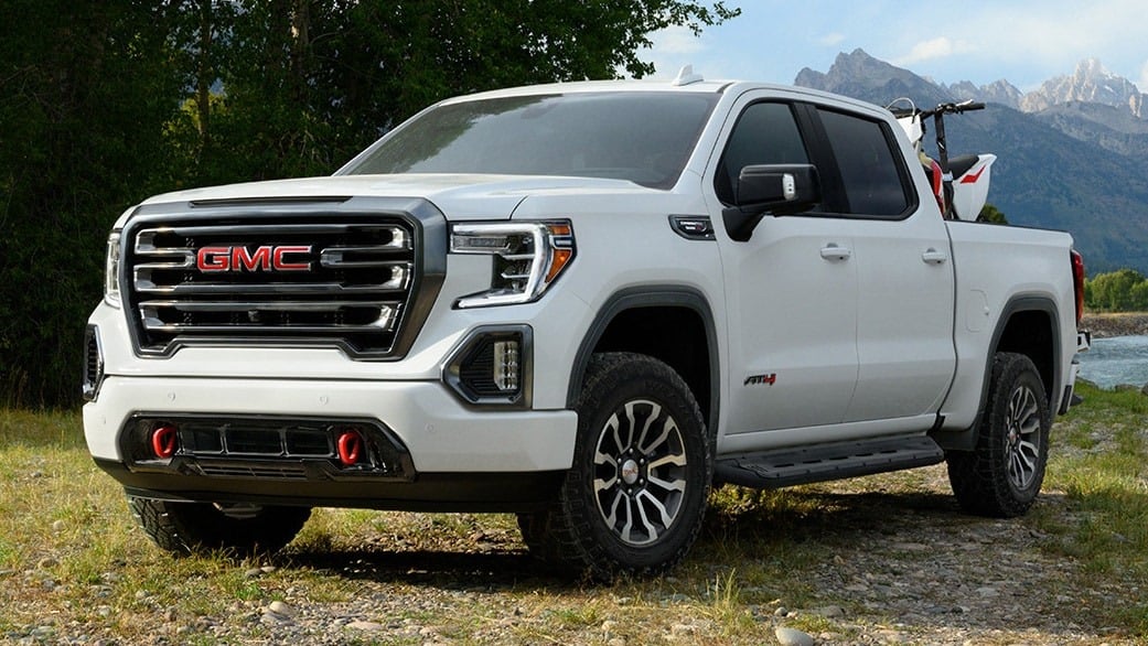 White GMC pickup truck parked outdoors with mountains and trees in the background.