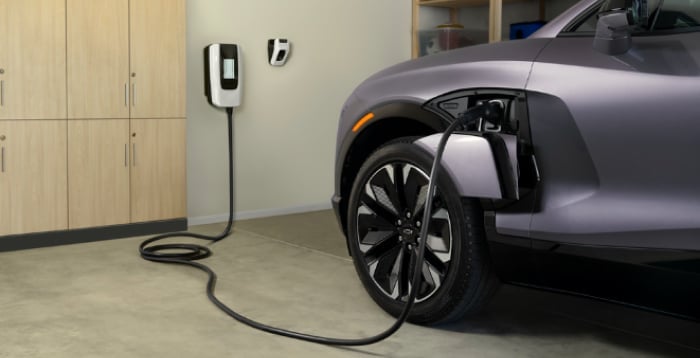 Electric car charging in a garage with a wall-mounted charger next to cabinets.