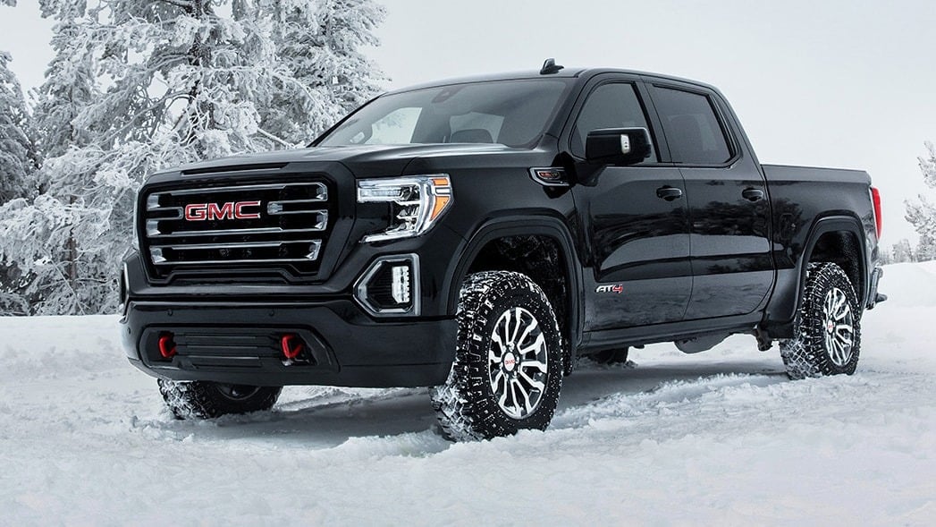 Black GMC pickup truck on snowy terrain with snow-covered trees in the background.